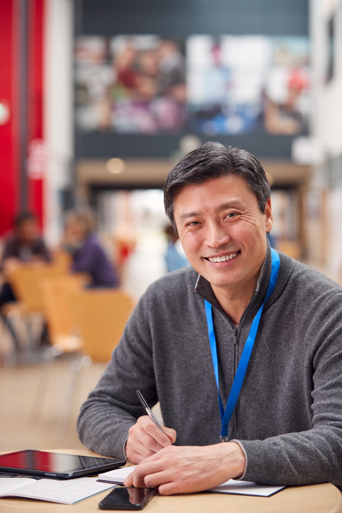 Portrait Of Mature Male Teacher Or Student With Digital Tablet Working At Table In College Hall